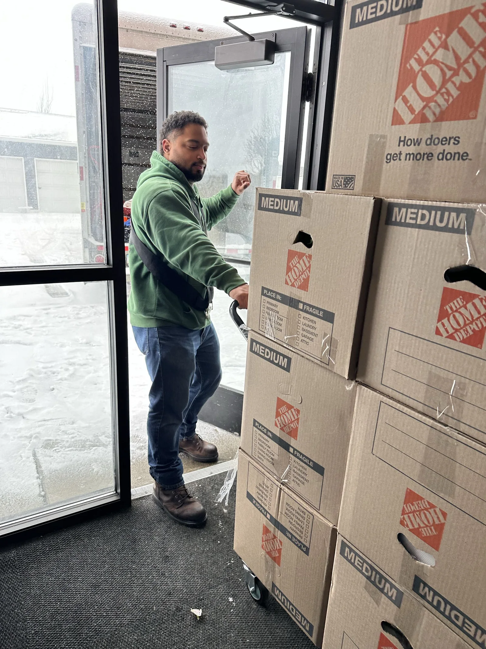 A crew member pushes stacked moving boxes on a hand truck.